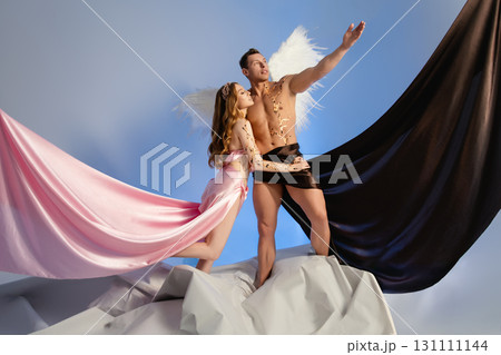 Couple dressed as angels pose dramatically against a vibrant blue backdrop Couple dressed as angels pose dramatically against a vibrant blue backdrop 131111144