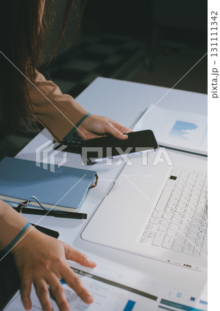 Close-up of businessman's hands making notes, mobiles, chart, desk, office Close-up of businessman's hands making notes, mobiles, chart, desk, office 131111342