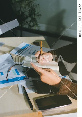 Close-up of businessman's hands making notes, mobiles, chart, desk, office 131111372