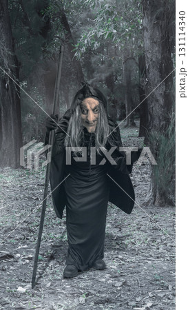 Old witch woman walking through the forest with a stick. The scene is scary and creepy. Concept of Spooky Halloween 131114340