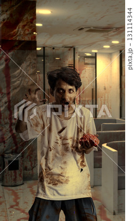 Scary male zombie with a wound and blood carrying a bloody brain on the abandoned building. The scene is scary and creepy. Concept of Spooky Halloween 131114344
