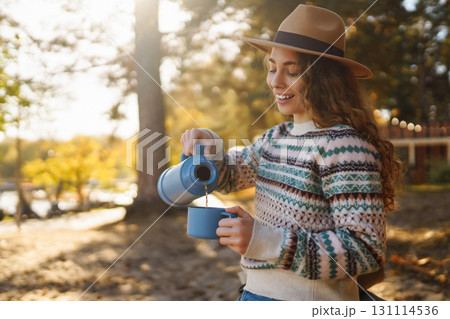 Lady drinks from thermo mug of coffee in nature. Warm up in sunny autumn forest. Travel, adventure. 131114536