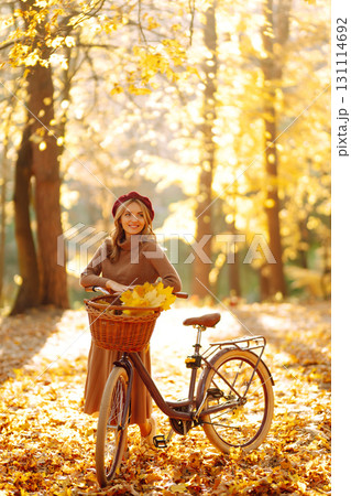 Stylish woman with a bicycle enjoying autumn weather in the park. Beautiful Woman in the autumn forest. 131114692