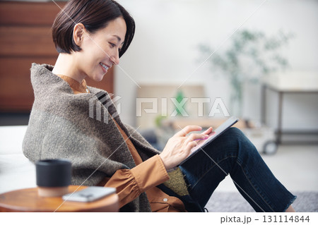 自宅でリラックスしながらタブレットを見ている40代女性 131114844