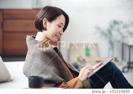 自宅でリラックスしながらタブレットを見ている40代女性 自宅でリラックスしながらタブレットを見ている40代女性 131114850
