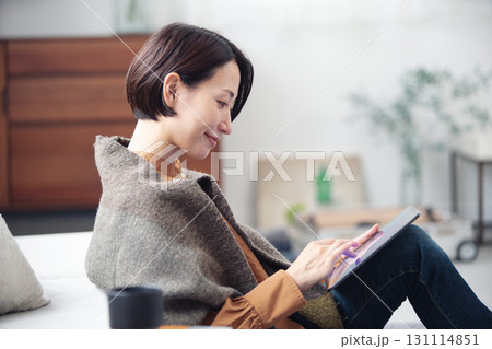自宅でリラックスしながらタブレットを見ている40代女性 131114851