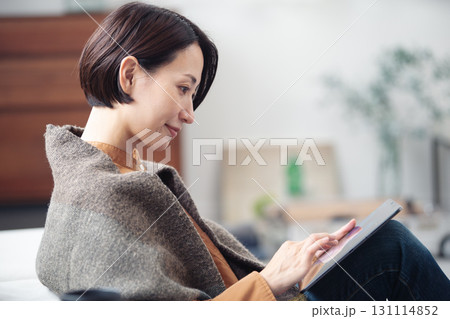 自宅でリラックスしながらタブレットを見ている40代女性 131114852