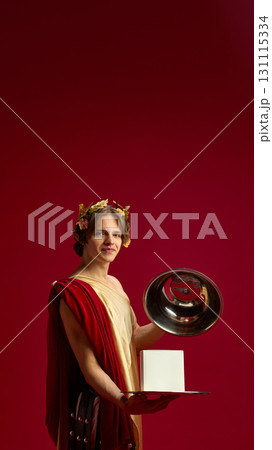 Young man in toga smiling with silver tray and blank box for creative presentation 131115334