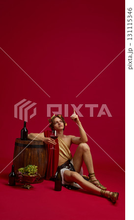 Young man in toga raising finger while holding wine glass in antique style 131115346