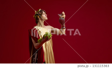 Young man in toga holding grapes and antique jug with proud look Young man in toga holding grapes and antique jug with proud look 131115363