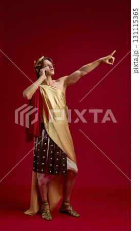 Young man in toga talking on phone with pointing gesture 131115365