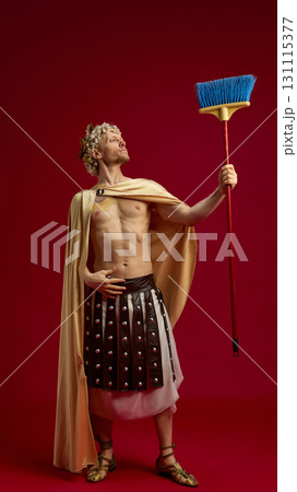 Man in Caesar costume holding broom like symbolic scepter on red background 131115377
