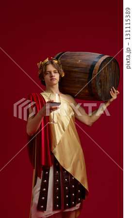 Young man in ancient toga carrying large wooden barrel and holding wine glass Young man in ancient toga carrying large wooden barrel and holding wine glass 131115389