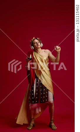 Man in ancient toga dancing with headphones and wine glass 131115402