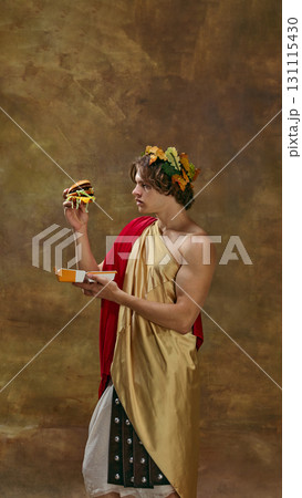 Young man in toga with laurel crown holding modern burger in packaging Young man in toga with laurel crown holding modern burger in packaging 131115430