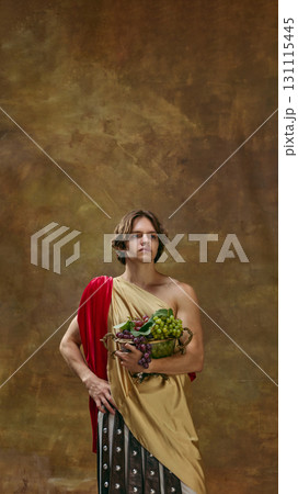 Young man in toga holding bowl of grapes with confident pose 131115445
