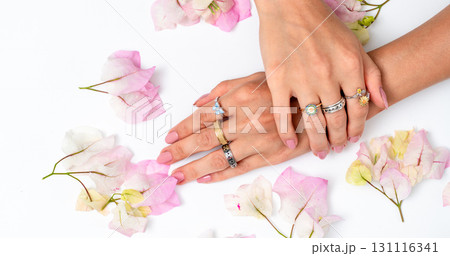 Elegant female hands with multiple rings and jewelry surrounded by pink flowers on white background Elegant female hands with multiple rings and jewelry surrounded by pink flowers on white background 131116341