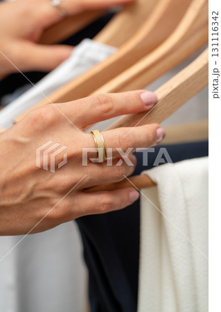 Close up of woman choosing clothes on wooden hangers in wardrobe or fashion store Close up of woman choosing clothes on wooden hangers in wardrobe or fashion store 131116342