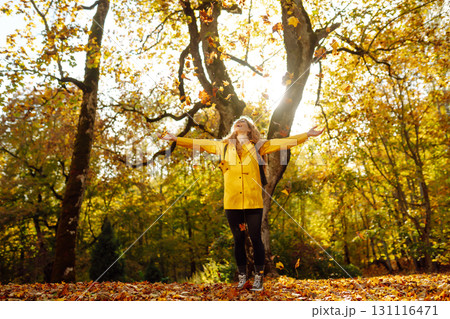 Happy female hiker in yellow coat walking in golden autumn forest. Woman has fun in autumn in park. Happy female hiker in yellow coat walking in golden autumn forest. Woman has fun in autumn in park. 131116471