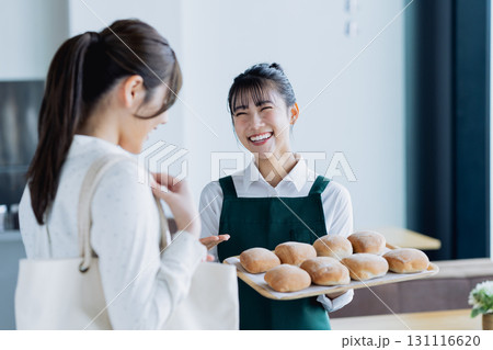 焼き立てパンをお客様に勧める若い女性の店員 焼き立てパンをお客様に勧める若い女性の店員 131116620