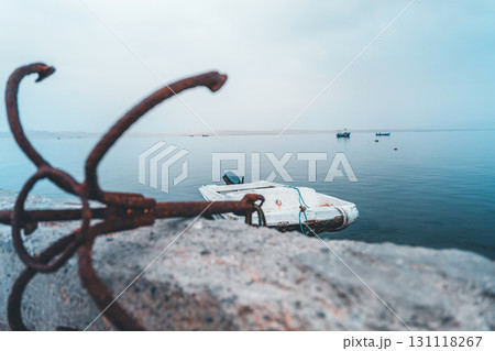 A boat is sitting on the water next to a rusty anchor A boat is sitting on the water next to a rusty anchor 131118267