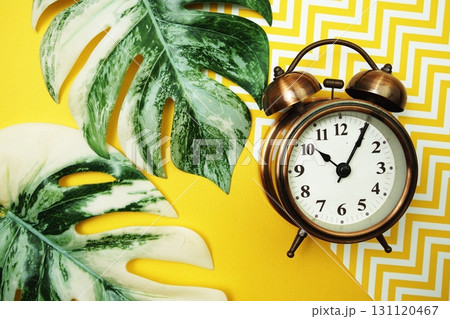 Alarm clock with Monstera Leaves on yellow background Alarm clock with Monstera Leaves on yellow background 131120467