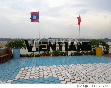 Riverside Plaza with Large Greenery Sign and Flags Under a Cloudy Sky by the Water Riverside Plaza with Large Greenery Sign and Flags Under a Cloudy Sky by the Water 131121746