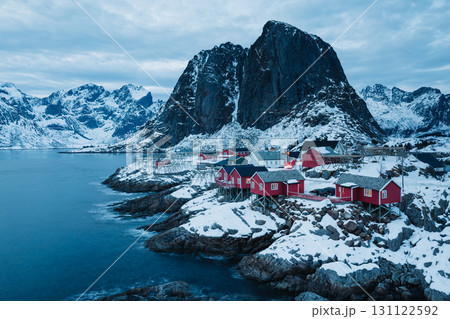 Red cabins in a snowy Norwegian village nestled by the sea and mountains.. Red cabins in a snowy Norwegian village nestled by the sea and mountains.. 131122592