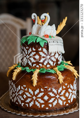 Rustic Wedding Cake with Two Swans Topper, Brown Layered Kulich with Icing Decoration, Easter Dessert, Celebration, Detailed Pastry Art. Rustic Wedding Cake with Two Swans Topper, Brown Layered Kulich with Icing Decoration, Easter Dessert, Celebration, Detailed Pastry Art. 131123270