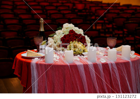 Romantic Dinner Setup on Theater Stage: Red Seats, Champagne, Wine, Roses, Cake, Candles, Elegant Celebration Scene 131123272