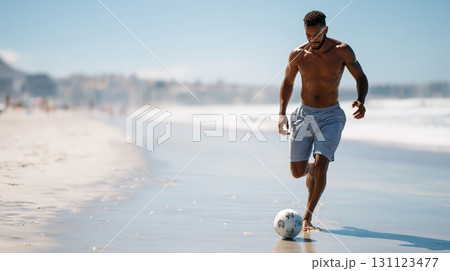 Man plays soccer on sandy beach during sunny day near ocean waves 131123477