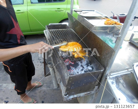 A Person Grilling a Large Squid on a Charcoal Grill at a Street Food Stand in the Day 131123657