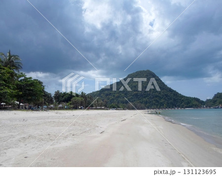A Quiet Sandy Beach with a Lush Green Mountain Under a Cloudy Sky in a Tropical Setting A Quiet Sandy Beach with a Lush Green Mountain Under a Cloudy Sky in a Tropical Setting 131123695