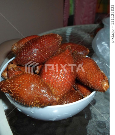 A White Bowl Filled with Spiky Red Fruits on a Table Ready for Enjoyment 131123833