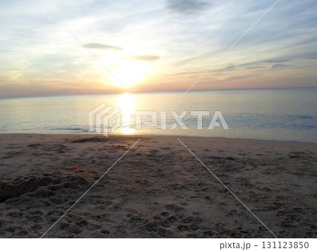 A Solitary Beach at Sunset with a Radiant Sun and Gentle Waves Under a Wispy Sky 131123850