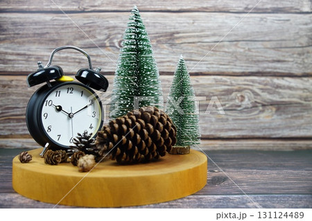 Winter-themed decor with a vintage alarm clock, pinecones, and miniature snowy trees on a wooden surface Winter-themed decor with a vintage alarm clock, pinecones, and miniature snowy trees on a wooden surface 131124489