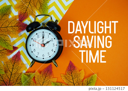 Daylight Saving Time with alarm clock and maple leaf decorated on orange background Daylight Saving Time with alarm clock and maple leaf decorated on orange background 131124517