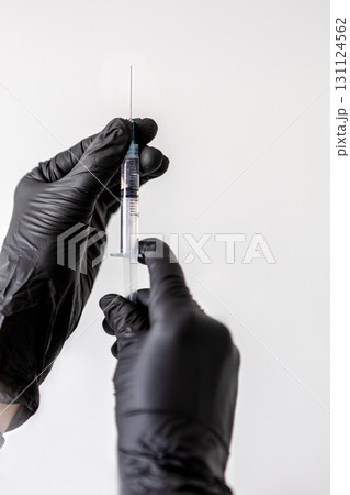 Doctors hands in black gloves holding syringe with needle. Medical professional preparing injection for vaccination, cosmetology or healthcare treatment on white background 131124562