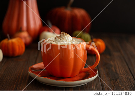 Cozy pumpkin latte in a pumpkin-shaped mug with whipped cream and spices, surrounded by autumn decor. Cozy pumpkin latte in a pumpkin-shaped mug with whipped cream and spices, surrounded by autumn decor. 131124830