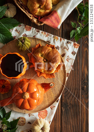 Autumnal tea set with pumpkin-shaped teapot and mug, and a baked bun on a wooden table. Top view. Copy space Autumnal tea set with pumpkin-shaped teapot and mug, and a baked bun on a wooden table. Top view. Copy space 131124838