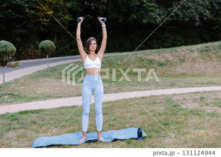 Young woman lifting weights during outdoor workout in a park 131124944