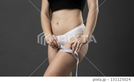 Woman measuring thigh with white tape while wearing sports underwear indoors 131125024