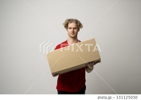 Young man in red t-shirt holding cardboard box on neutral studio background 131125030