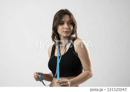 Woman in black sportswear holding measuring tape around neck indoors Woman in black sportswear holding measuring tape around neck indoors 131125047