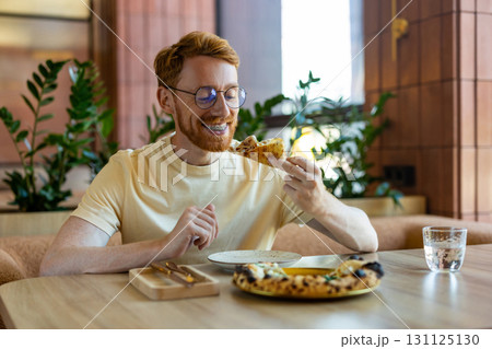 Bearded man in yellow shirt sitting at cafe table with pizza 131125130