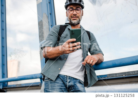 City commuter standing by bike, reading text message on phone. City commuter standing by bike, reading text message on phone. 131125258