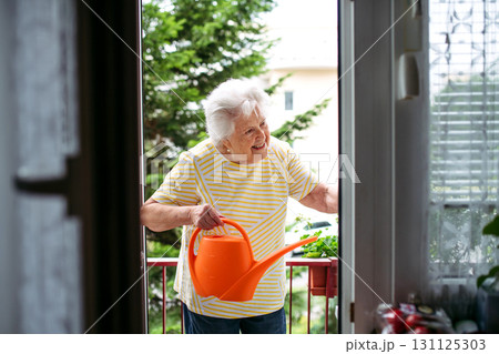 Elderly woman watering potted flowers on balcony. Elderly woman watering potted flowers on balcony. 131125303