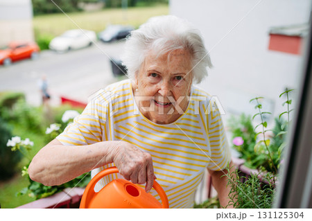 Elderly woman watering potted flowers on balcony. Elderly woman watering potted flowers on balcony. 131125304