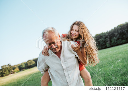 Grandfather playing with granddaughter on meadow. 131125317