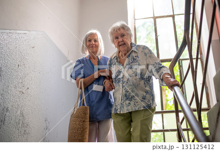Female healthcare worker helping senior patient walking down the stairs. Female healthcare worker helping senior patient walking down the stairs. 131125412